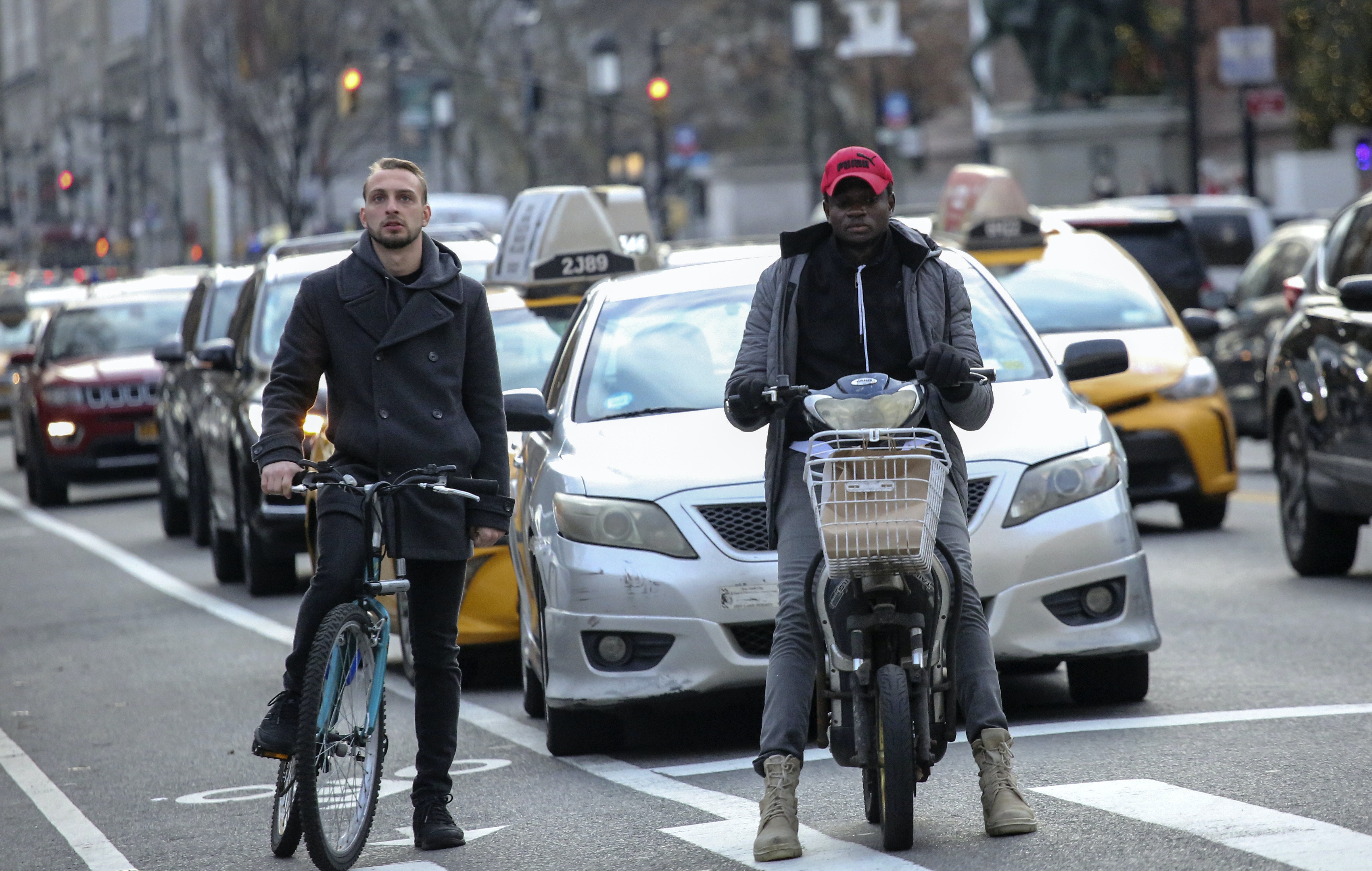 Two men on bicycles wait with taxis at a city stoplight.