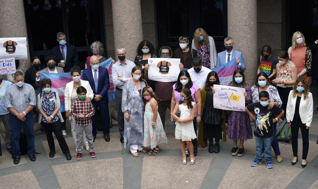 Parents and children wearing masks and holding signs protesting anti-transgender legislation