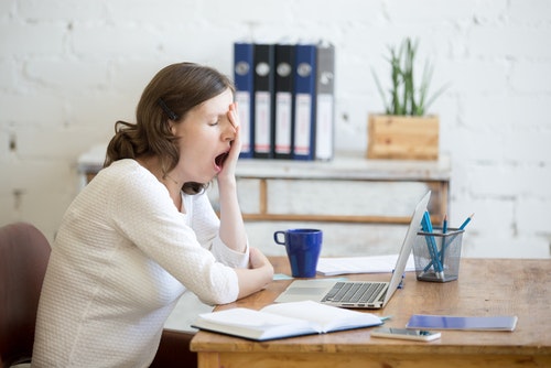 woman at laptop yawns and rubs face