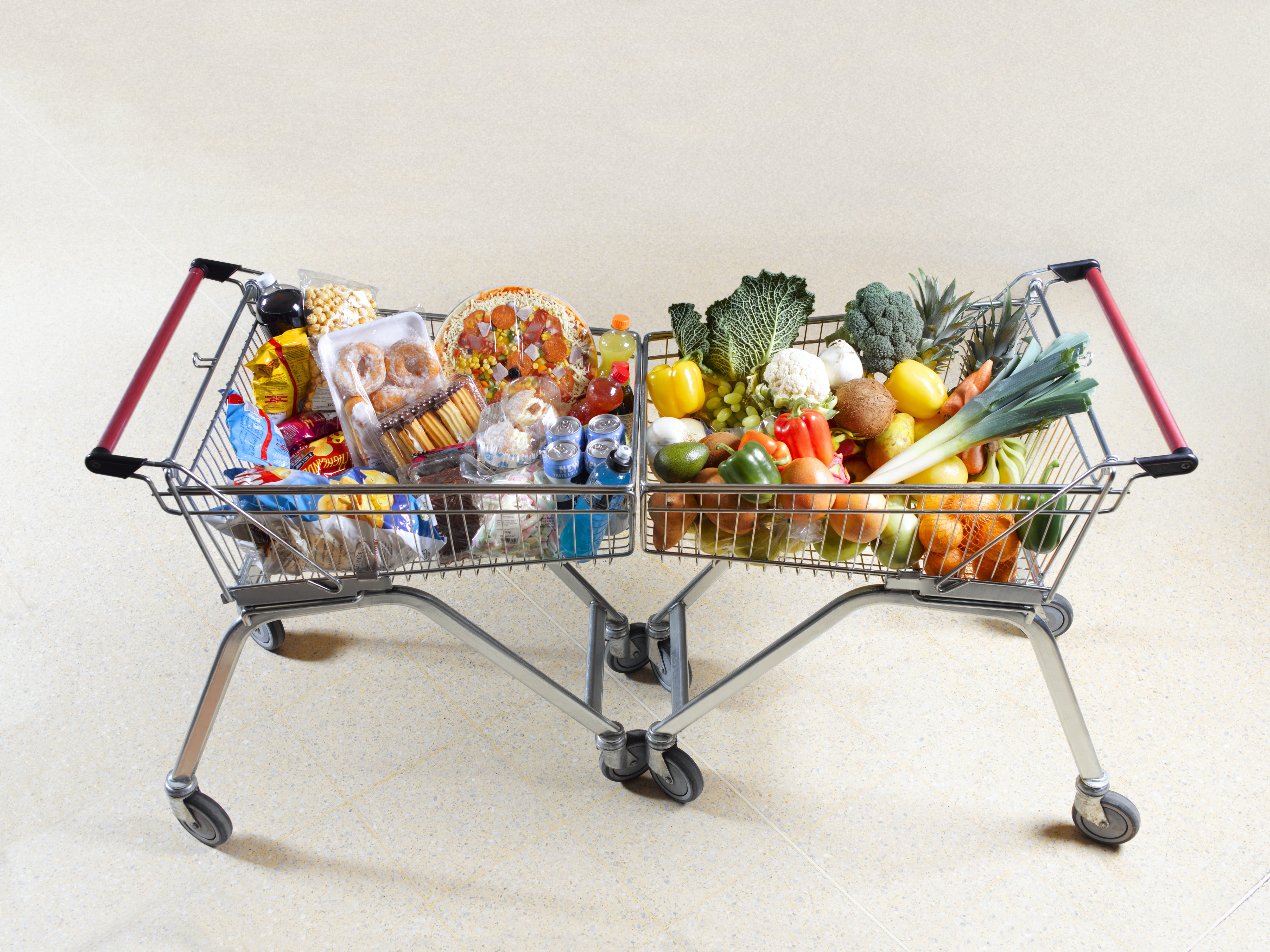 Two shopping carts lined up, one filled with fruits and vegetables, the other with sweets and high-fat foods.