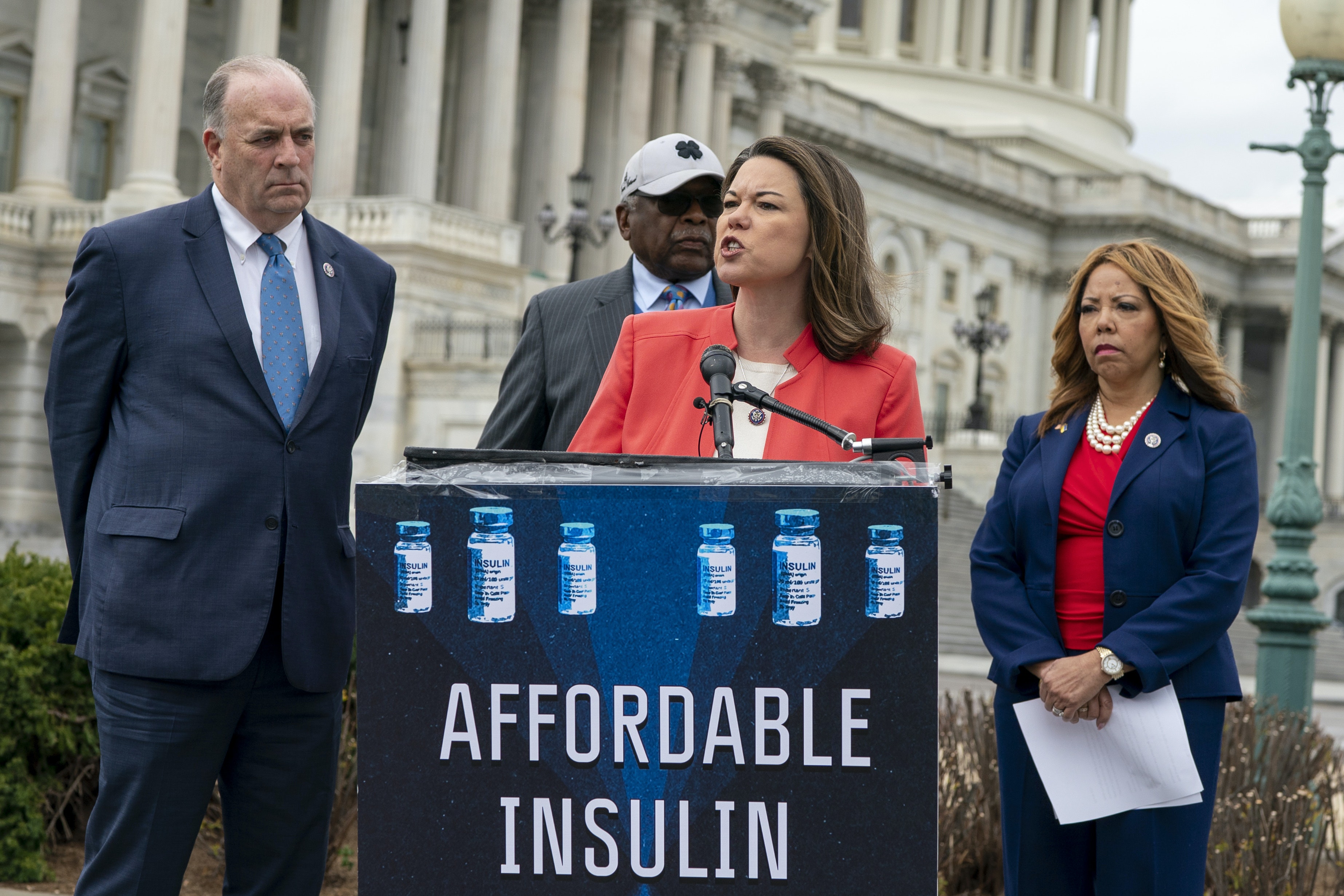Two women and two men in suits next to an 'affordable insulin' sign in front of the U.S. Capitol building.