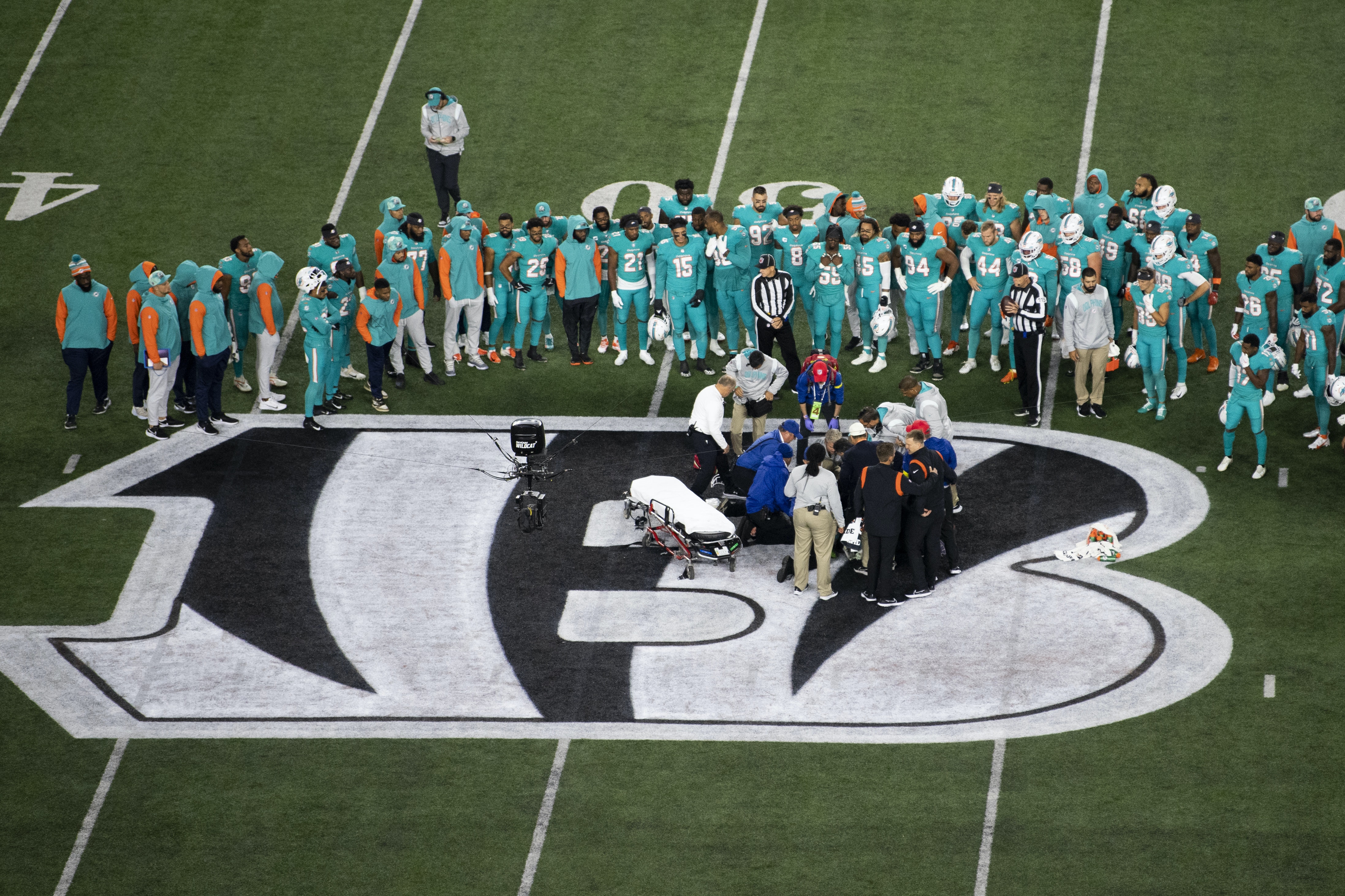 Football players stand in a circle looking at a teammate stretched on the ground.