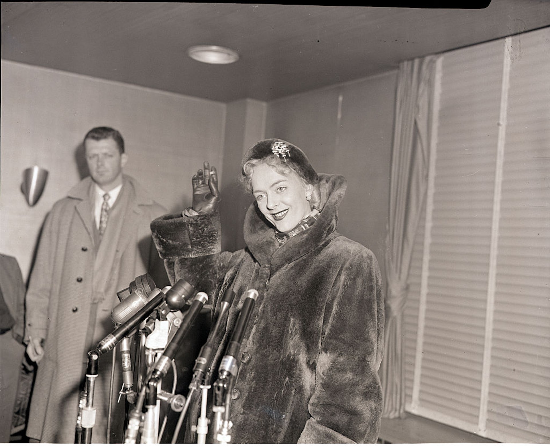 Christine Jorgensen standing before a set of microphones at a press conference