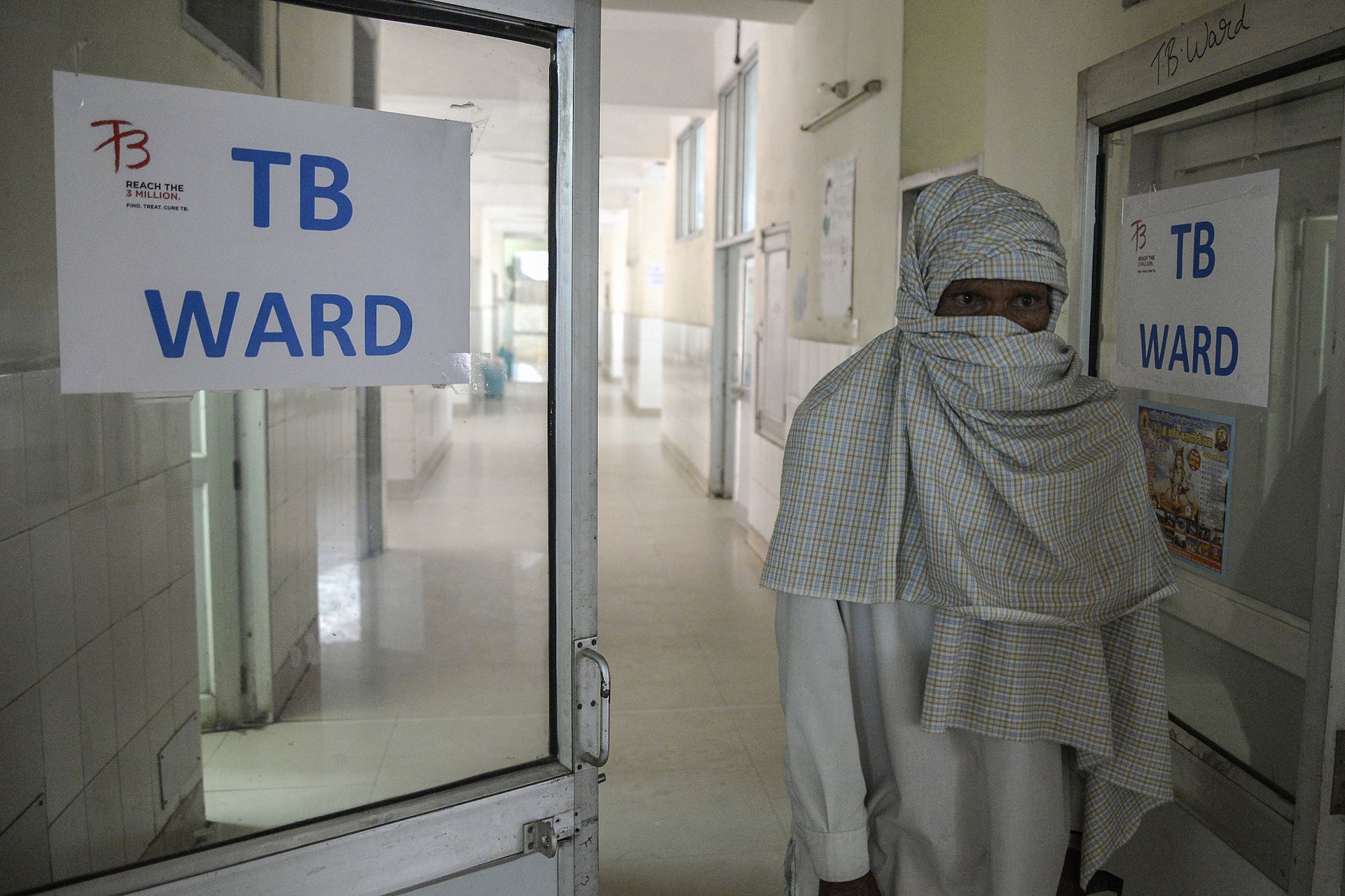 An man standing in a hospital next to a sign with TB Ward written on it.