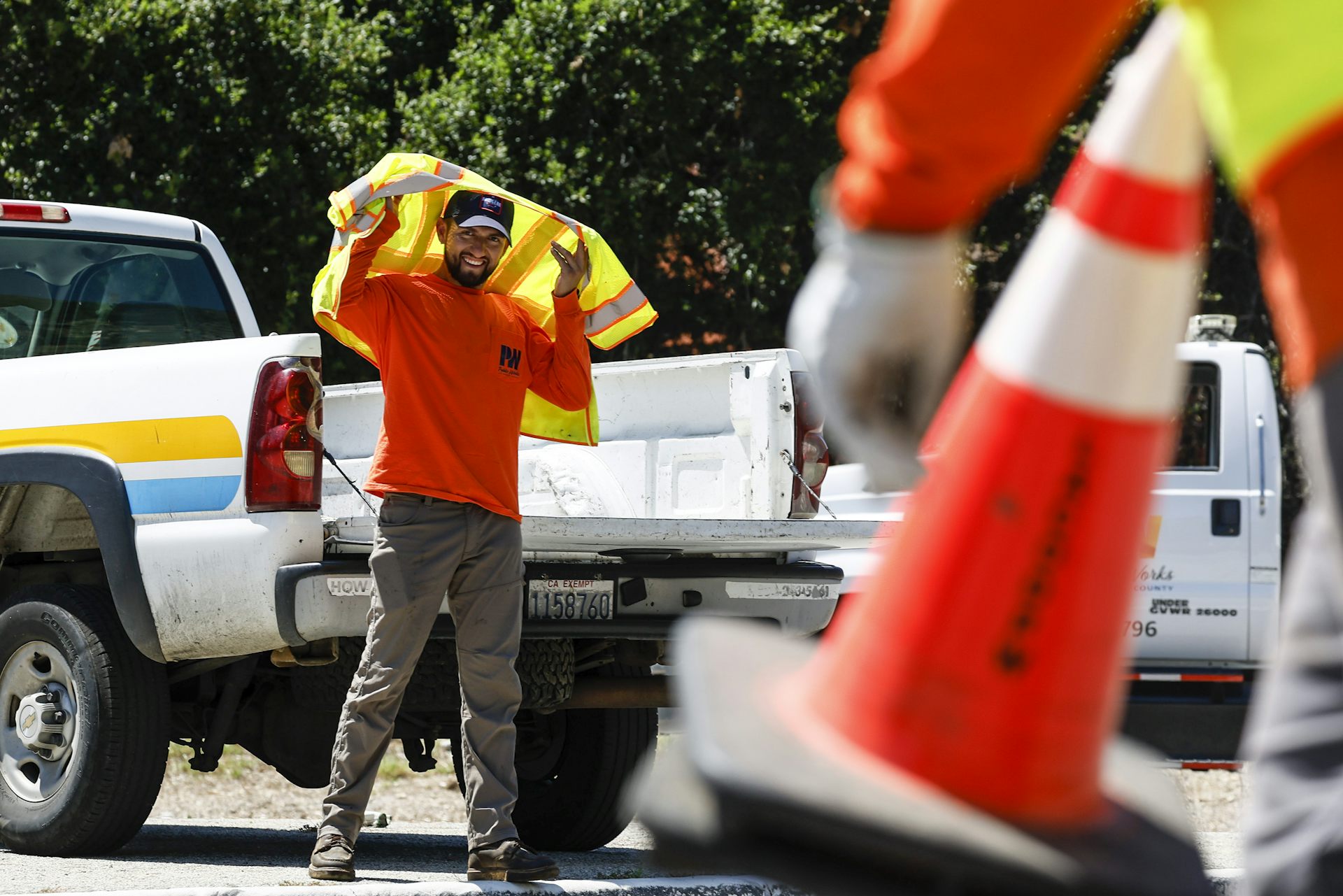 A construction worker in reflective gear holds a jacket over his head against the sun.