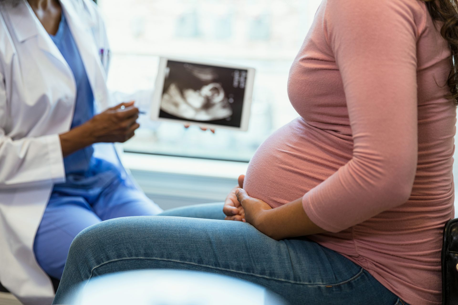 Pregnant person talks with medical profession with ultrasound image in background