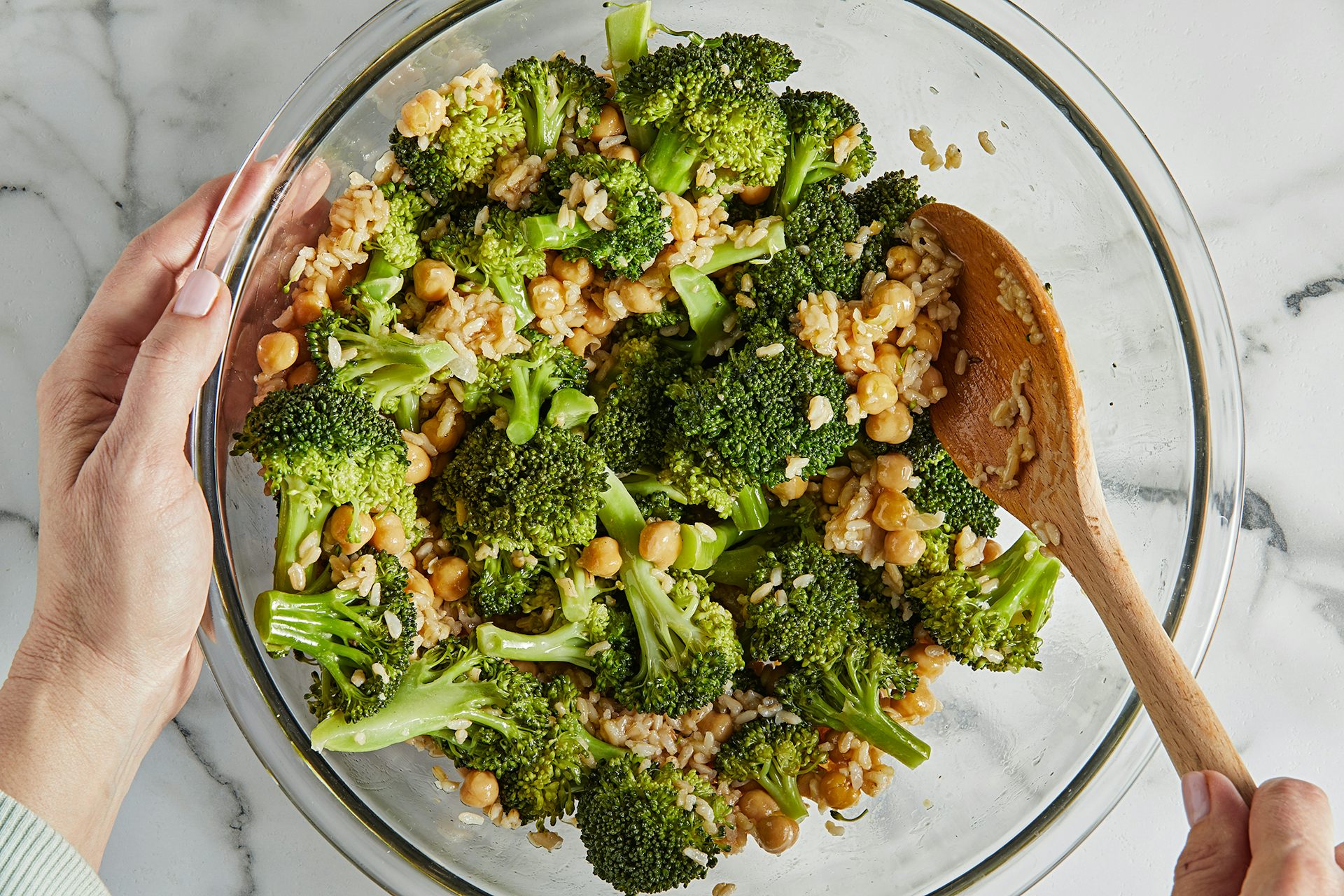 A bowl of warm broccoli, chickpea and rice salad with a wooden spoon in it.