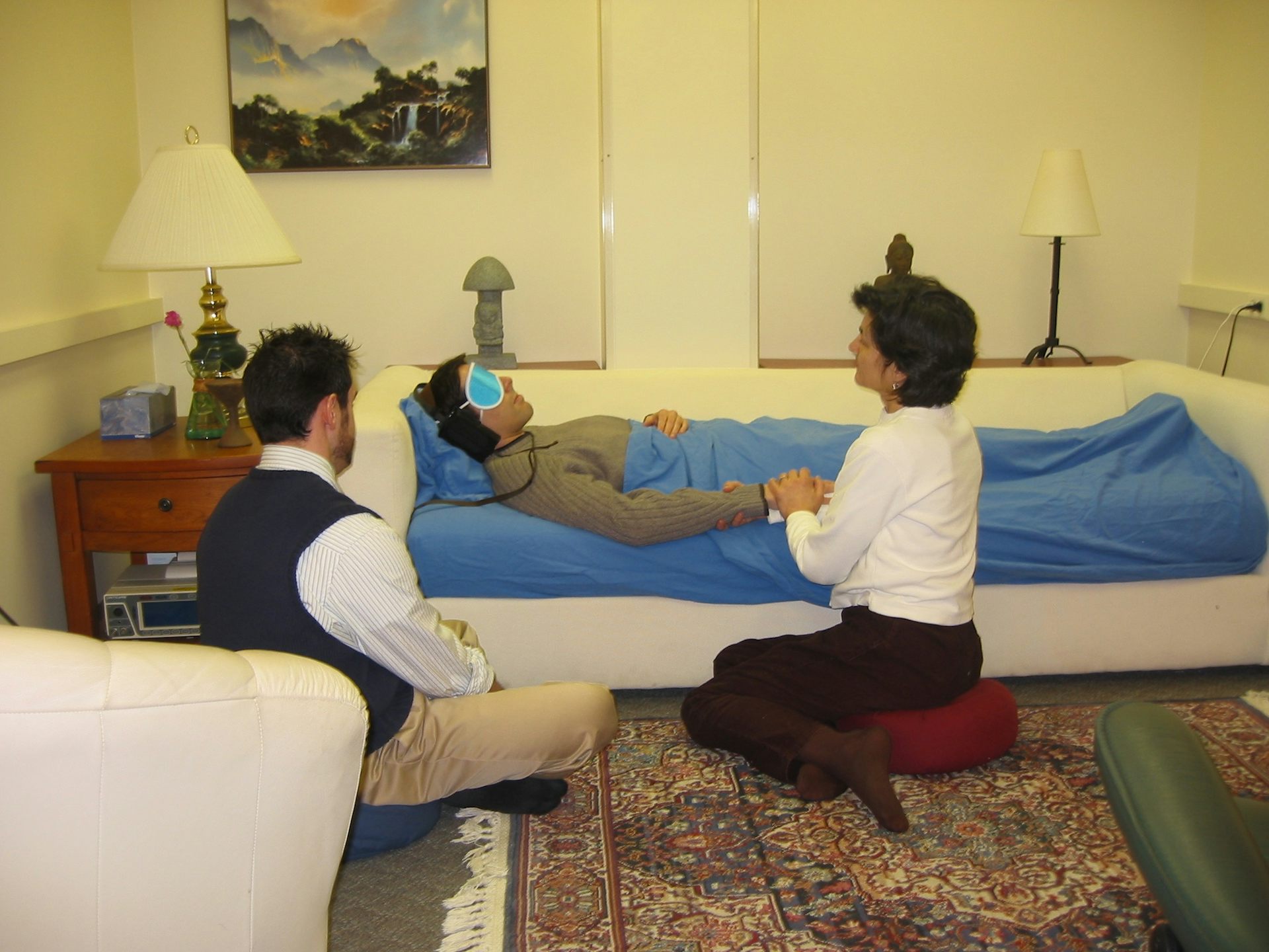 Two people sitting next to a couch, where a man on psilocybin is lying down.