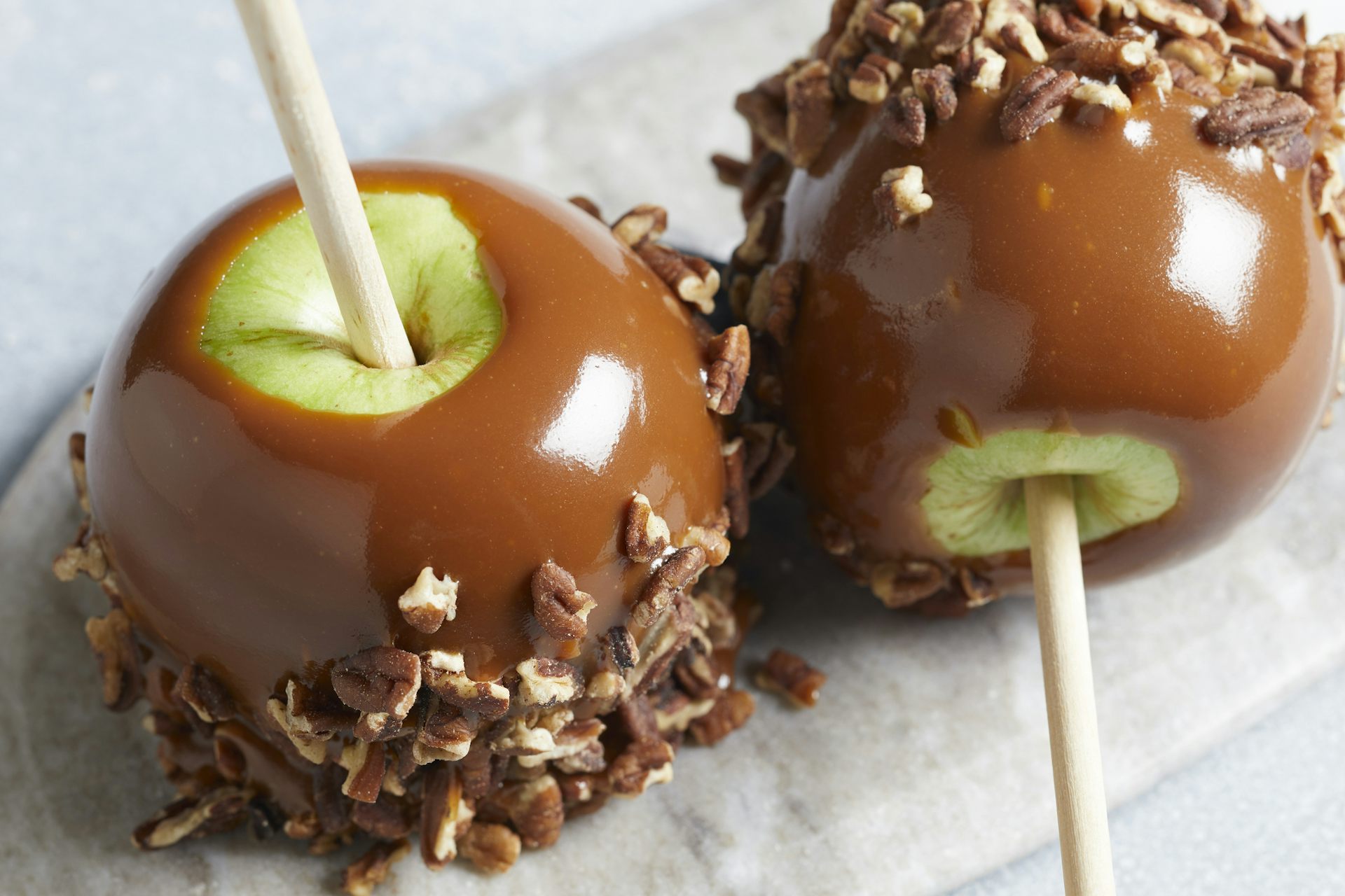 Two green apples on a stick, coated in caramel and dusted with pecans.