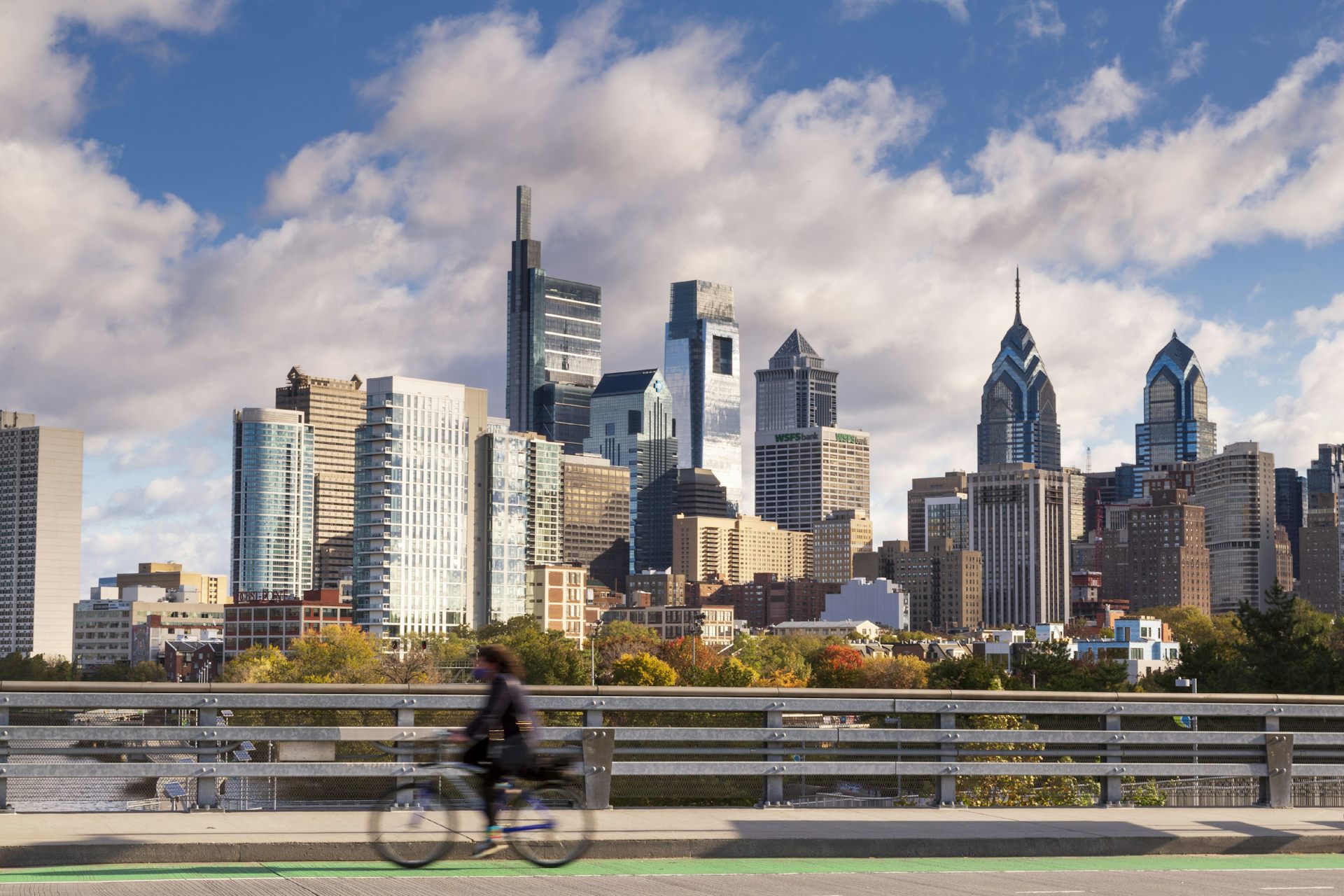 Blurred cyclist seen riding past Philly skyline on sunny, blue-sky day