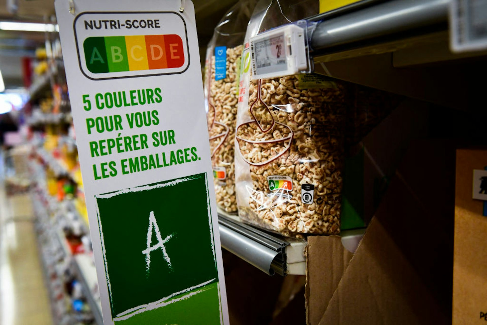 Sign hanging off shelf of grocery store with letters A to E assigned green to red, the sign reading '5 couleurs pour vous réperer sur les emballages'