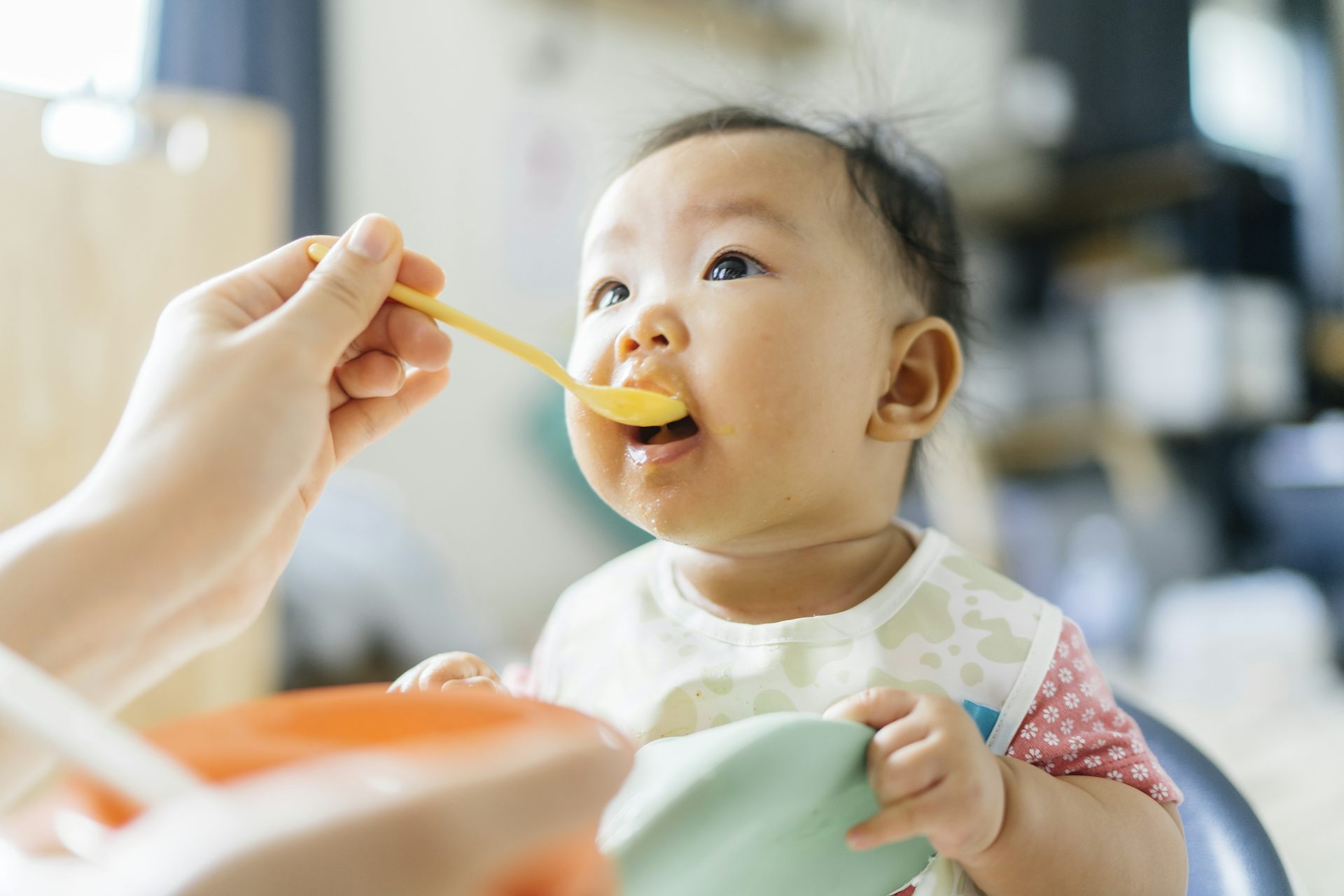 A hand holds a spoon of baby food to a baby's lips